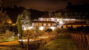 A large, multi-story house with a well-lit exterior, surrounded by a landscaped garden and a vineyard. - Casal dos Capelinhos - Quinta Nova (Santa Marta de Penaguião)