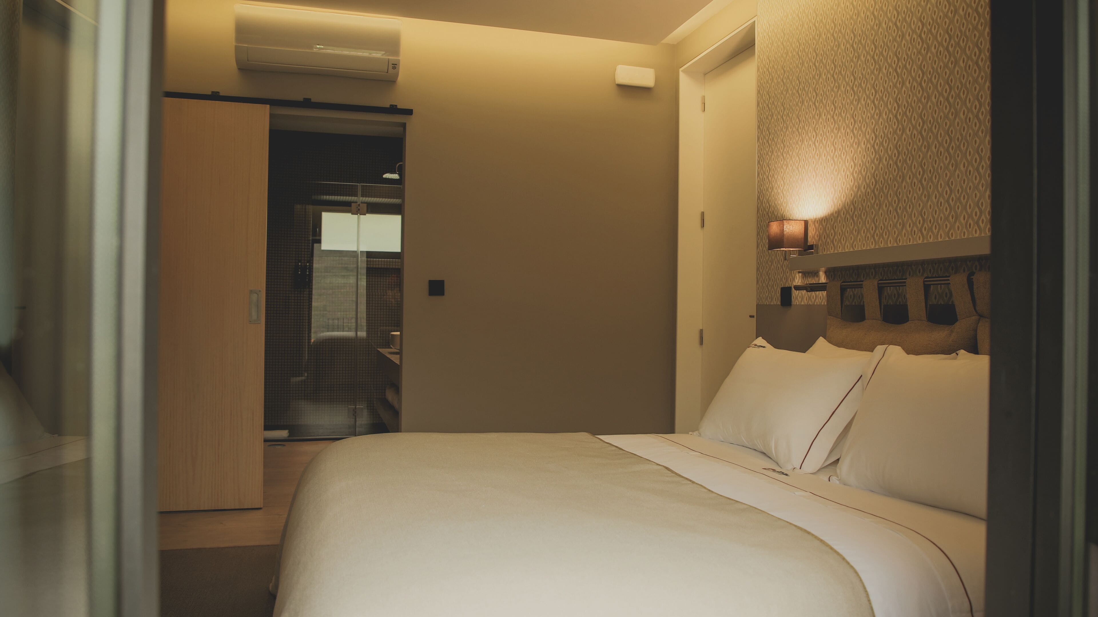 Ett hotellrum med en säng, en sänglampa, en garderob och ett badrum som syns genom en öppen dörr.