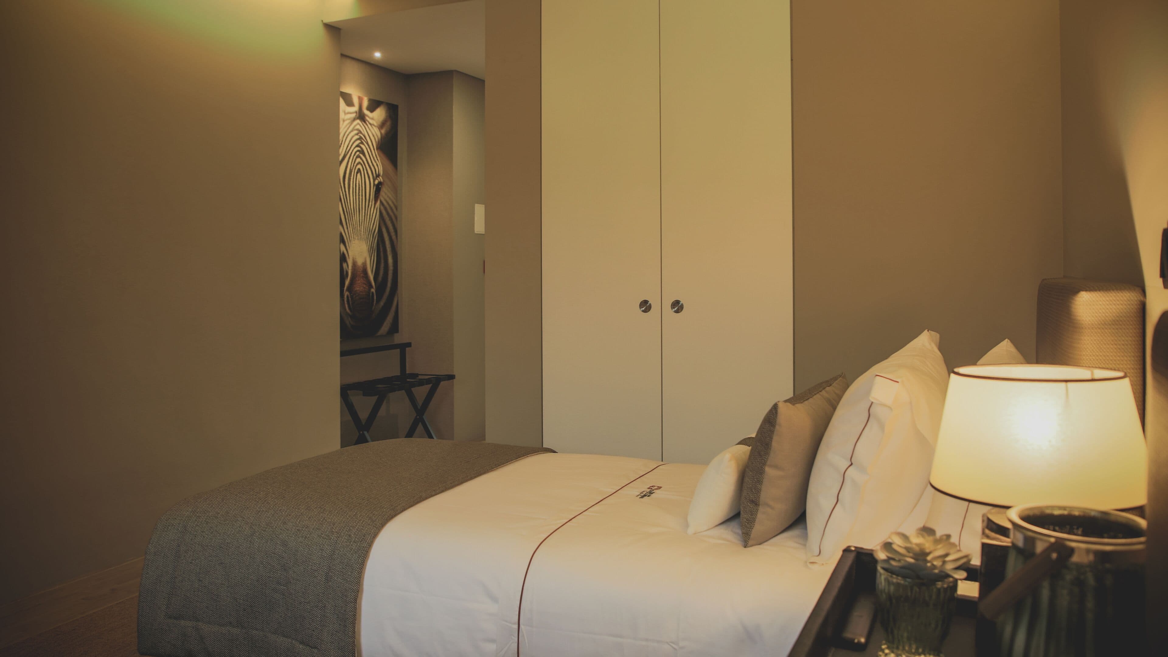 Et hotelværelse med seng, puder, en sengetavle, et lille bord og et skab.