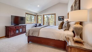 A bedroom with a large bed, a TV, a wooden cabinet, and three windows. - Summit Sanctuary | Beautiful Views | Hot Tub! (Breckenridge)