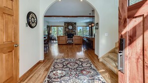 A spacious hallway with wooden flooring, a patterned rug, and a stone fireplace in the background. - Summit Sanctuary | Beautiful Views | Hot Tub! (Breckenridge)