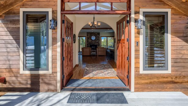 A wooden cabin with a central doorway leading to a living area with a fireplace, seating, and a view of the outdoors. - Summit Sanctuary | Beautiful Views | Hot Tub! (Breckenridge)