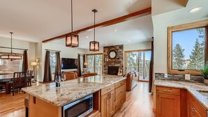 A spacious kitchen with a large island, wooden cabinets, and a stone fireplace. - Summit Sanctuary | Beautiful Views | Hot Tub! (Breckenridge)