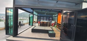 A modern outdoor terrace with glass walls, a seating area, and a view of the city and hills. - Penthouse Seaview Apartment On Patong Beach (Tambon Patong)