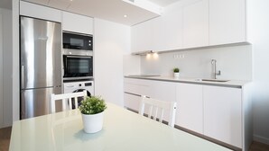 A modern kitchen with stainless steel appliances, white cabinetry, and a dining area with a glass table and chairs.