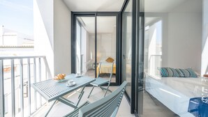 A balcony with a table and chairs, a sofa, and a glass door leading to an interior space.