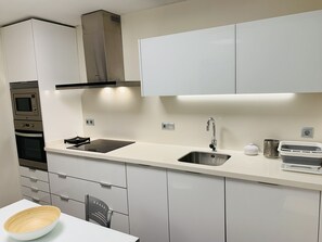 Une cuisine moderne avec des meubles blancs, un évier en acier inoxydable, un four encastré et une plaque de cuisson à induction noire.
