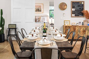 A dining room with a long table set for a meal, a clock on the wall, and a chalkboard with a welcome message. - Hot Tub • Sauna • Cold Plunge • 3 King Suites | Sedona Wellness Retreat (Sedona)