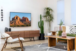 Un soggiorno moderno con una grande TV a schermo piatto, un tavolino in legno, una poltrona bianca, un divano verde e un cactus in vaso.