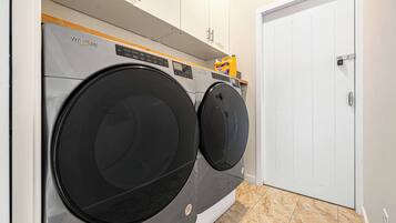 A laundry room with two front-loading Whirlpool washers, a white door, and a shelf with cleaning supplies.