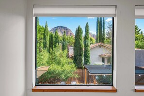 Une fenêtre donnant sur une montagne, des arbres et une maison.