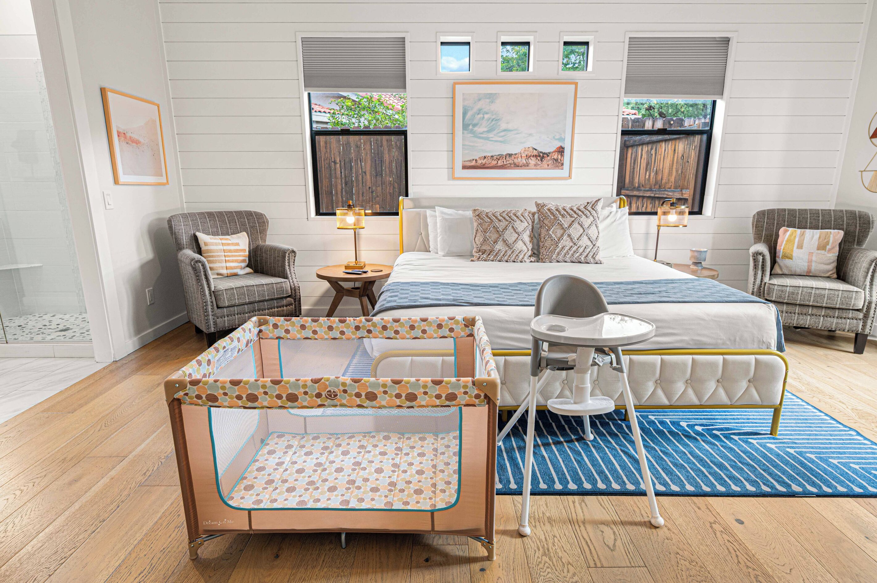 Habitación de hotel con cama, dos sillones, una mesita, cuna y ventana con vista a la vegetación.