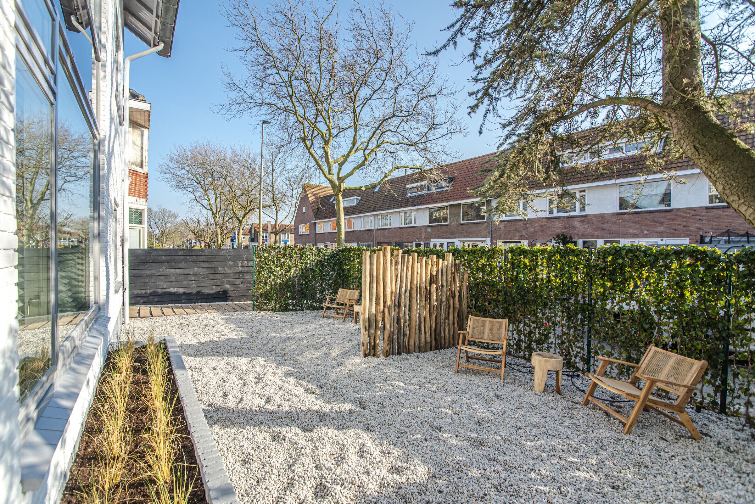 Ein Wohnbereich im Freien mit Kiesterrasse, Holzbanken, Holzzaun und einer Hecke.