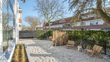 Ein Wohnbereich im Freien mit Kiesterrasse, Holzbanken, Holzzaun und einer Hecke.