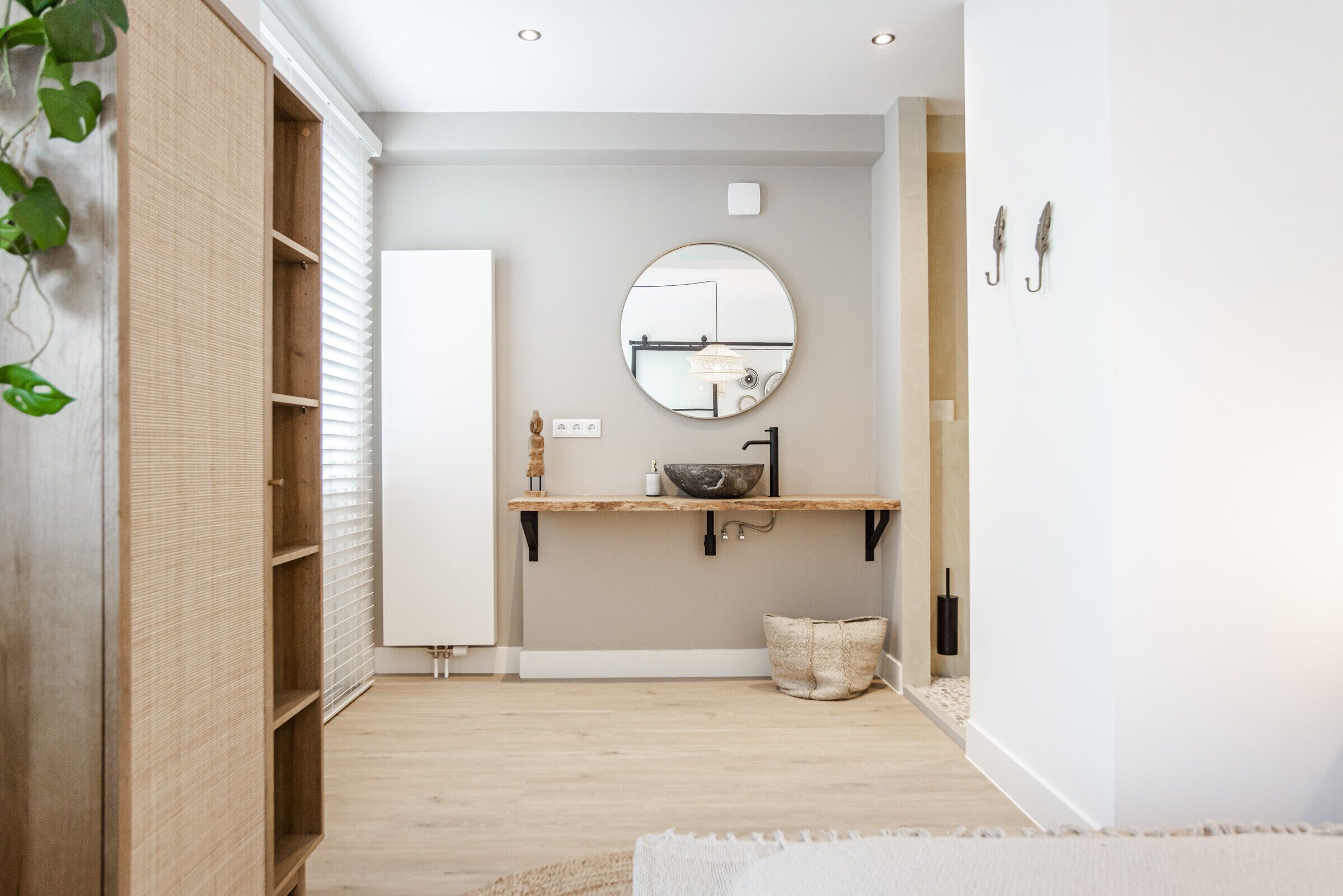 A modern bathroom with a wooden vanity, a round mirror, and a light fixture.