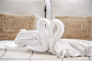 Ein ordentlich gefaltetes weißes Handtuch, das in Herzform auf einem Bett mit beigen Kissen drapiert ist.