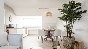 Un salon moderne avec un canapé, une table basse et un coin repas comprenant une table et des chaises. On y trouve une grande plante dans un pot en pierre et un luminaire suspendu.