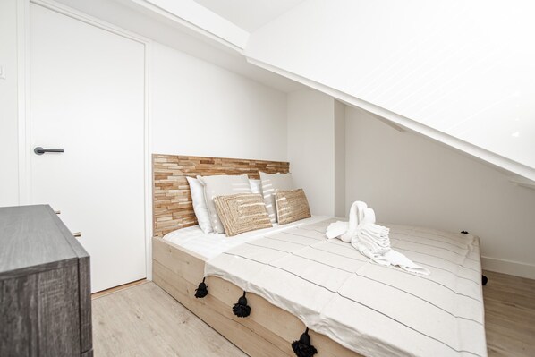 Un dormitorio con cabecera de madera, ropa de cama blanca y una mesita de noche pequeña.