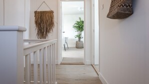 Un couloir avec une rambarde blanche, une décoration tissée suspendue et un sac à motifs accroché au mur.