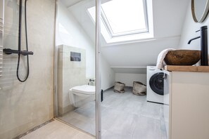 Ein modernes Badezimmer mit Duschkabine aus Glas, einem Oberlicht, einer Toilette, einer Waschmaschine und einem hölzernen Waschbecken.