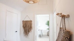 Un couloir avec une porte blanche, une décoration murale en macramé suspendue, un luminaire suspendu en fibres tressées et un grand sac à motifs accroché au mur.