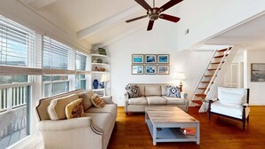 Ein geräumiges Wohnzimmer mit hohen Decken, einem Deckenventilator, einer Sofagarnitur, einem Couchtisch und einer Treppe, die in ein Obergeschoss führt.