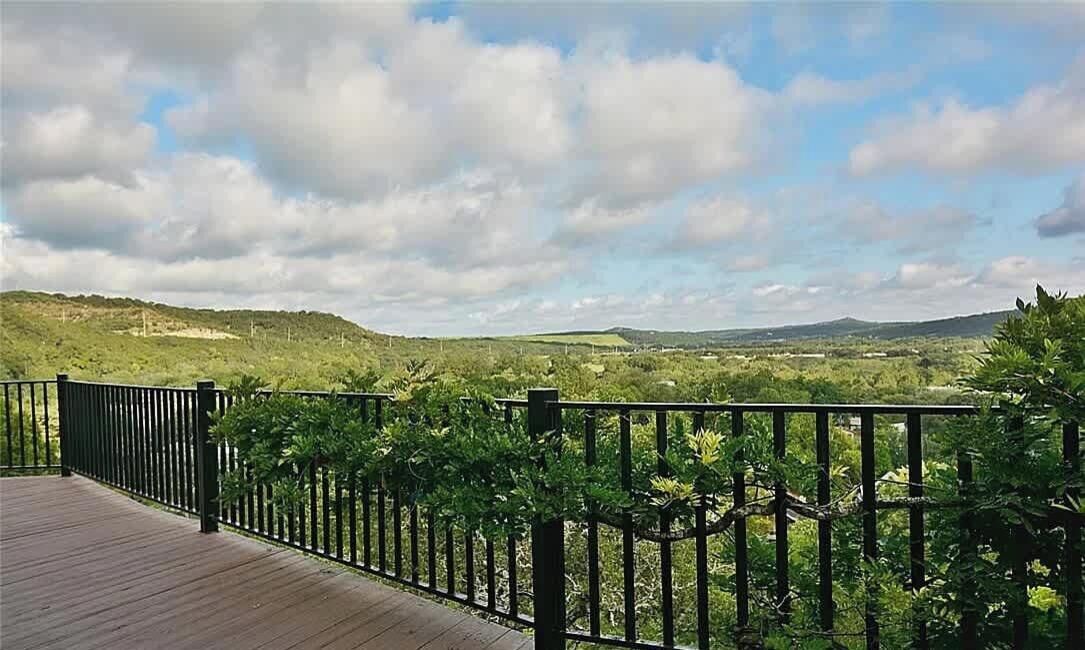 A wooden deck with a black railing overlooking a hilly landscape with trees and a clear sky.