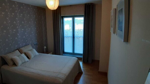 Une chambre à coucher avec un lit, une fenêtre avec des rideaux et un luminaire fixé au mur.