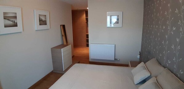 A bedroom with a bed, a dresser, a radiator, and framed pictures on the wall.