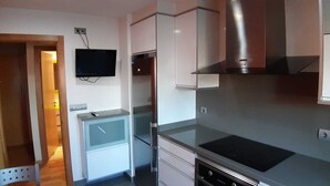 Une cuisine compacte équipée d’un four à micro-ondes encastré, d’une cuisinière et d’un petit réfrigérateur. Un téléviseur à écran plat est fixé au mur.