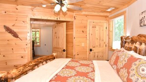 Une chambre dans une cabane en bois, avec un lit, un ventilateur de plafond et une fenêtre équipée de stores.