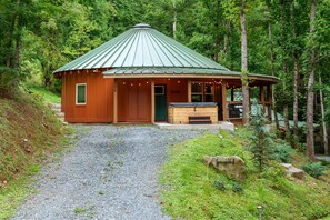 A rustic cabin with a green metal roof, a wooden door, and a small porch area. - Spicewood Yurt (Bryson City)