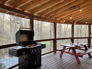 A covered outdoor area with a barbecue grill, picnic table, and wooden deck. - Spicewood Yurt (Bryson City)