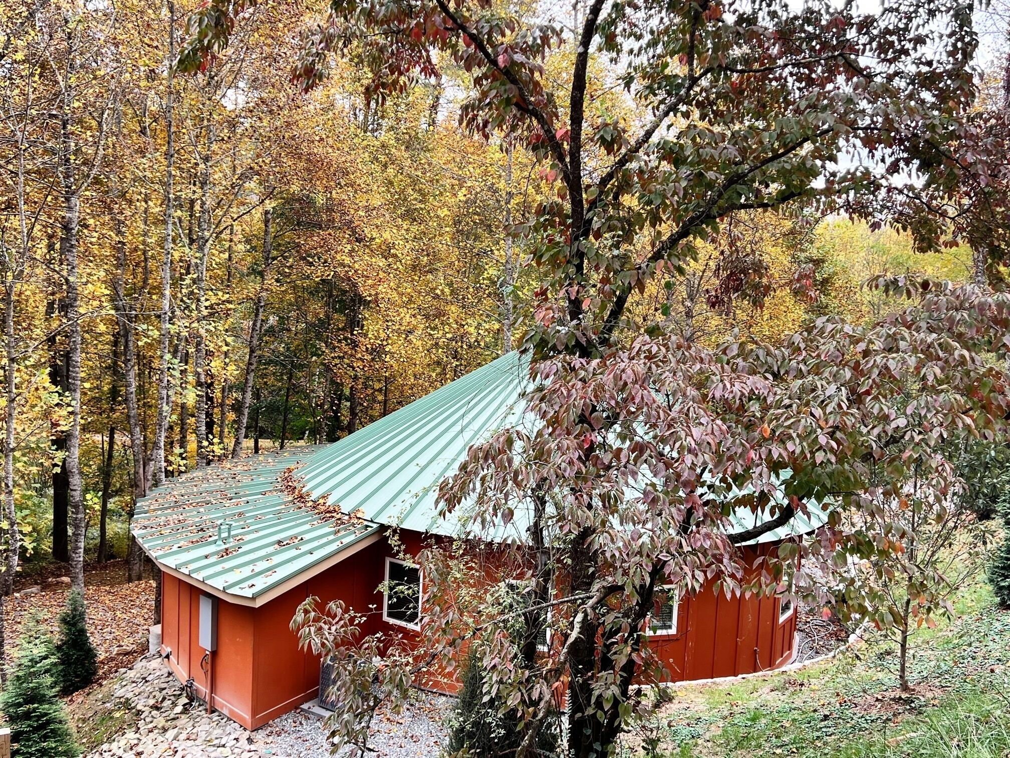 A small, red cabin with a green roof surrounded by autumn foliage.