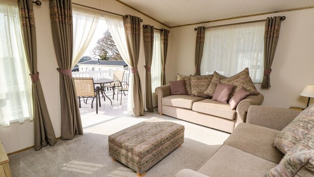 A cozy living room with a beige sofa, an ottoman, and a dining area with a table and chairs. - Crosswinds 68 (Bembridge)