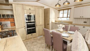 A modern kitchen with wooden cabinets, stainless steel appliances, and a dining area with a table set for two. - Crosswinds 68 (Bembridge)