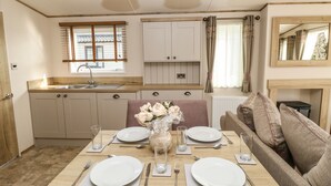 A dining area with a wooden table set for four, a sofa, and a kitchen in the background. - Crosswinds 68 (Bembridge)