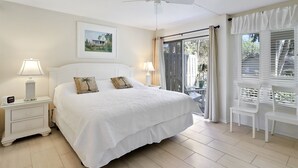 Een slaapkamer met een bed, twee nachtkastjes met lampen, een plafondventilator, een raam met gordijnen en uitzicht op buiten.