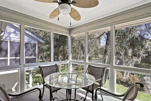 Une véranda avec une table en verre et quatre chaises, de grandes fenêtres et un ventilateur de plafond.