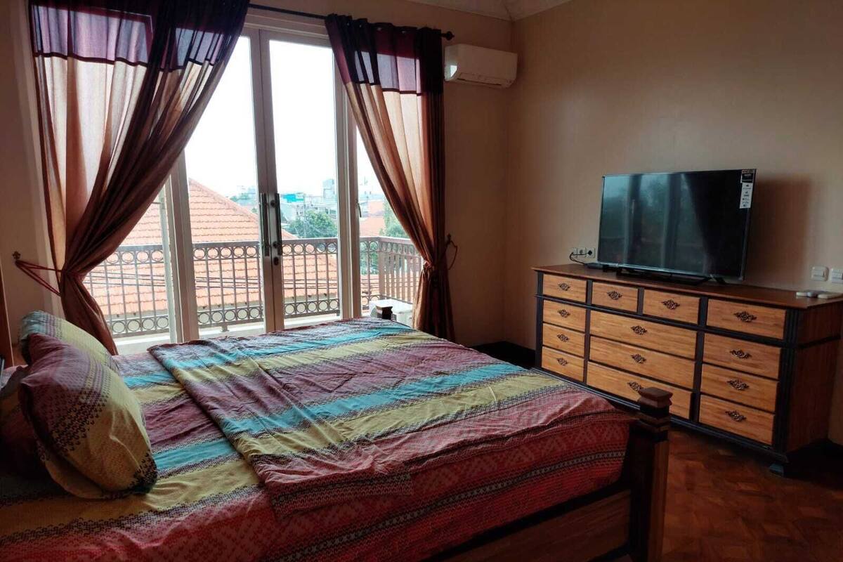 Een slaapkamer met een bed, een dressoir, een televisie en een raam met gordijnen.