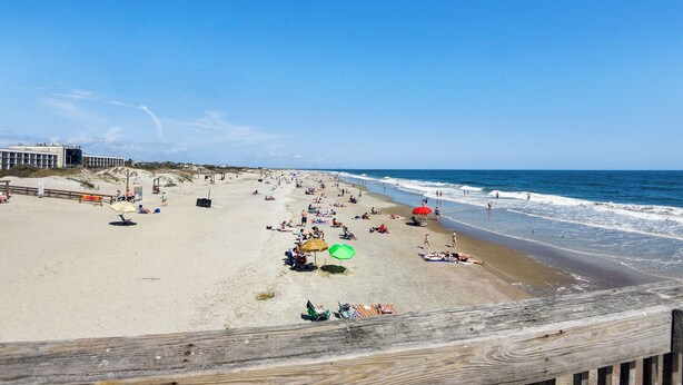 En strand med en träpromenad, sandstrand och vågor som slår in mot land.
