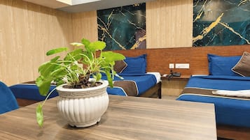 Habitación de hotel con cabecera de madera, cama con ropa de cama azul, mesita de noche con teléfono y planta en maceta sobre una mesa de madera.