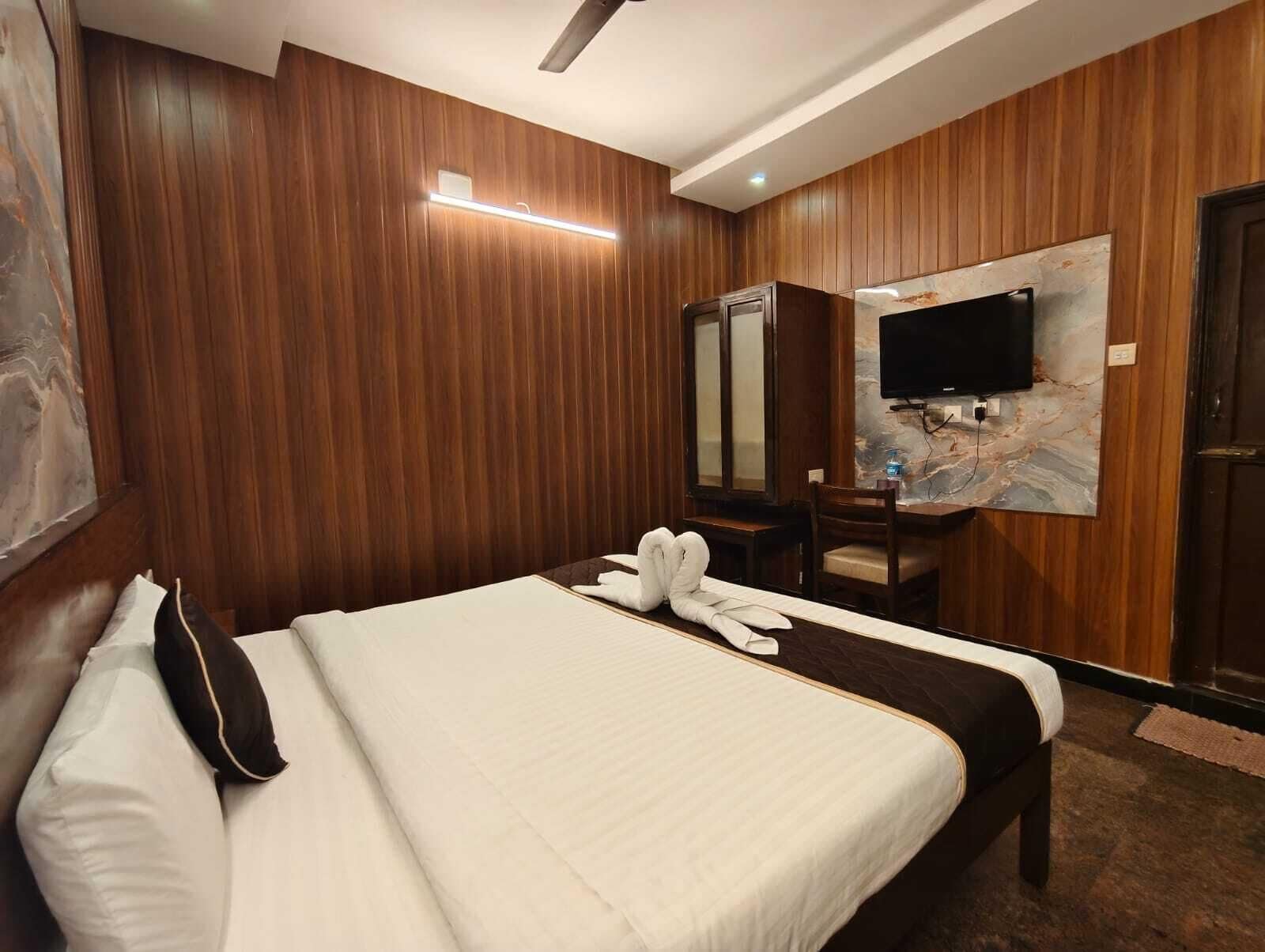 Una habitación de hotel con cama, escritorio, silla, televisor y espejo.