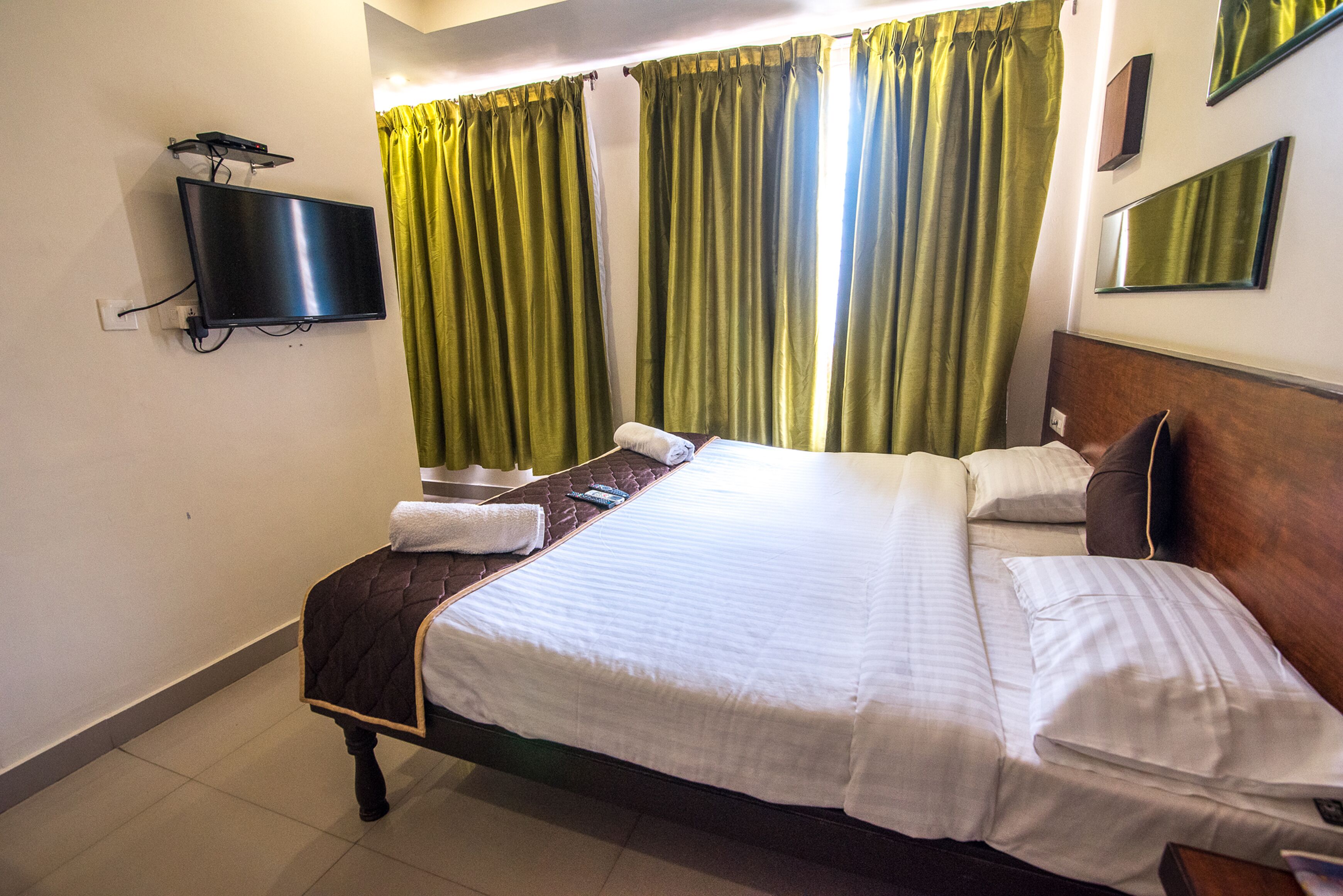 A hotel room with a bed, a television mounted on the wall, and curtains.