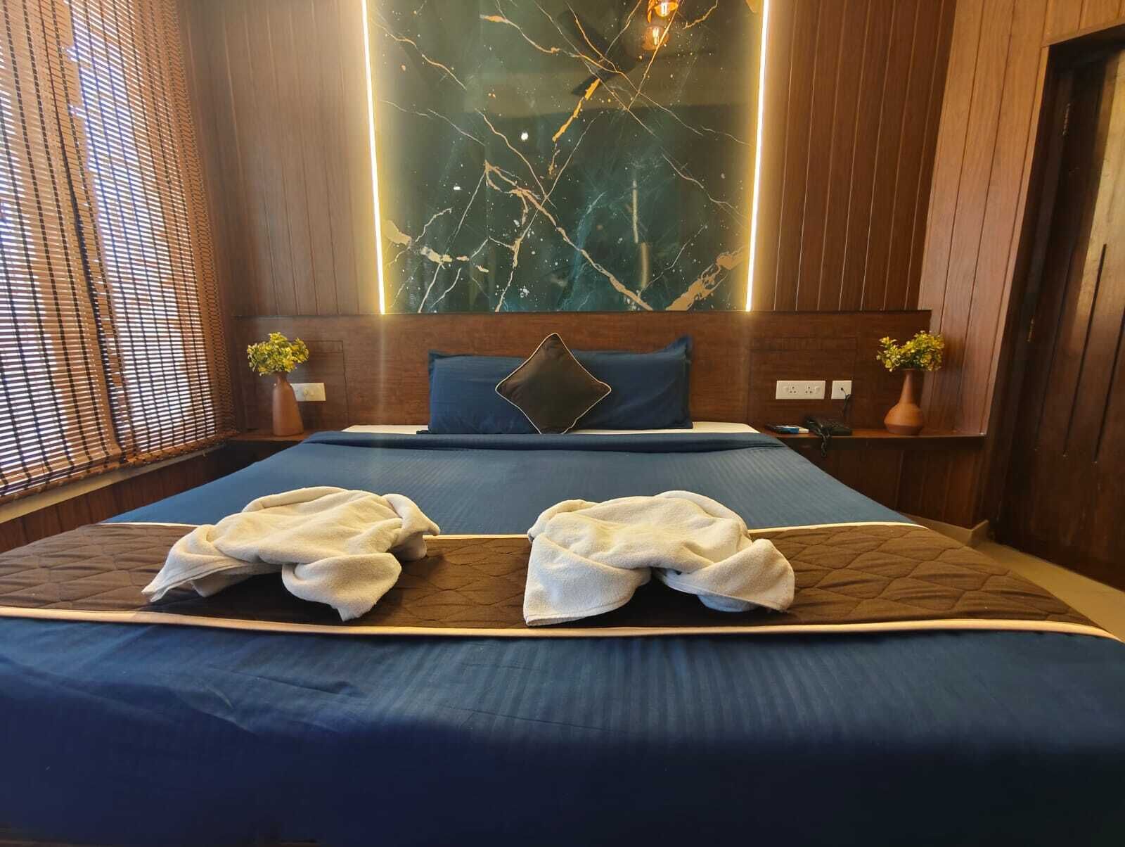 A hotel room with a large bed, a marble wall, wooden paneling, and two potted plants.