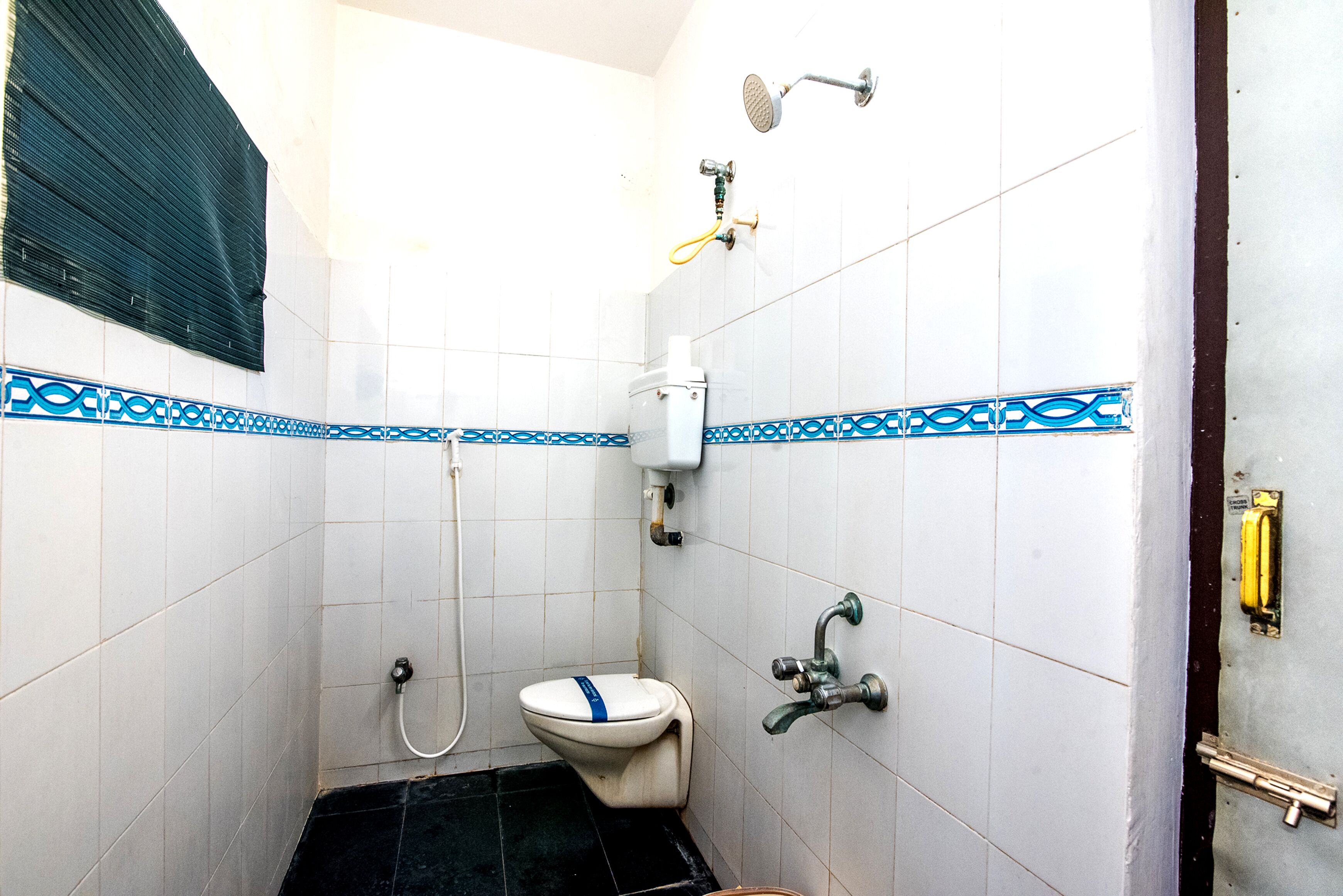 Une petite salle de bain carrelée, équipée de toilettes, d’une douche et d’un lavabo.