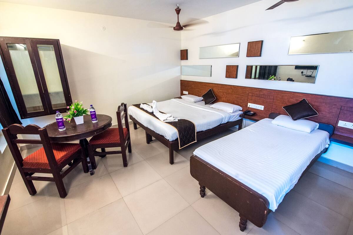A hotel room with two single beds, a wooden headboard, a desk with a chair, and a dining table.