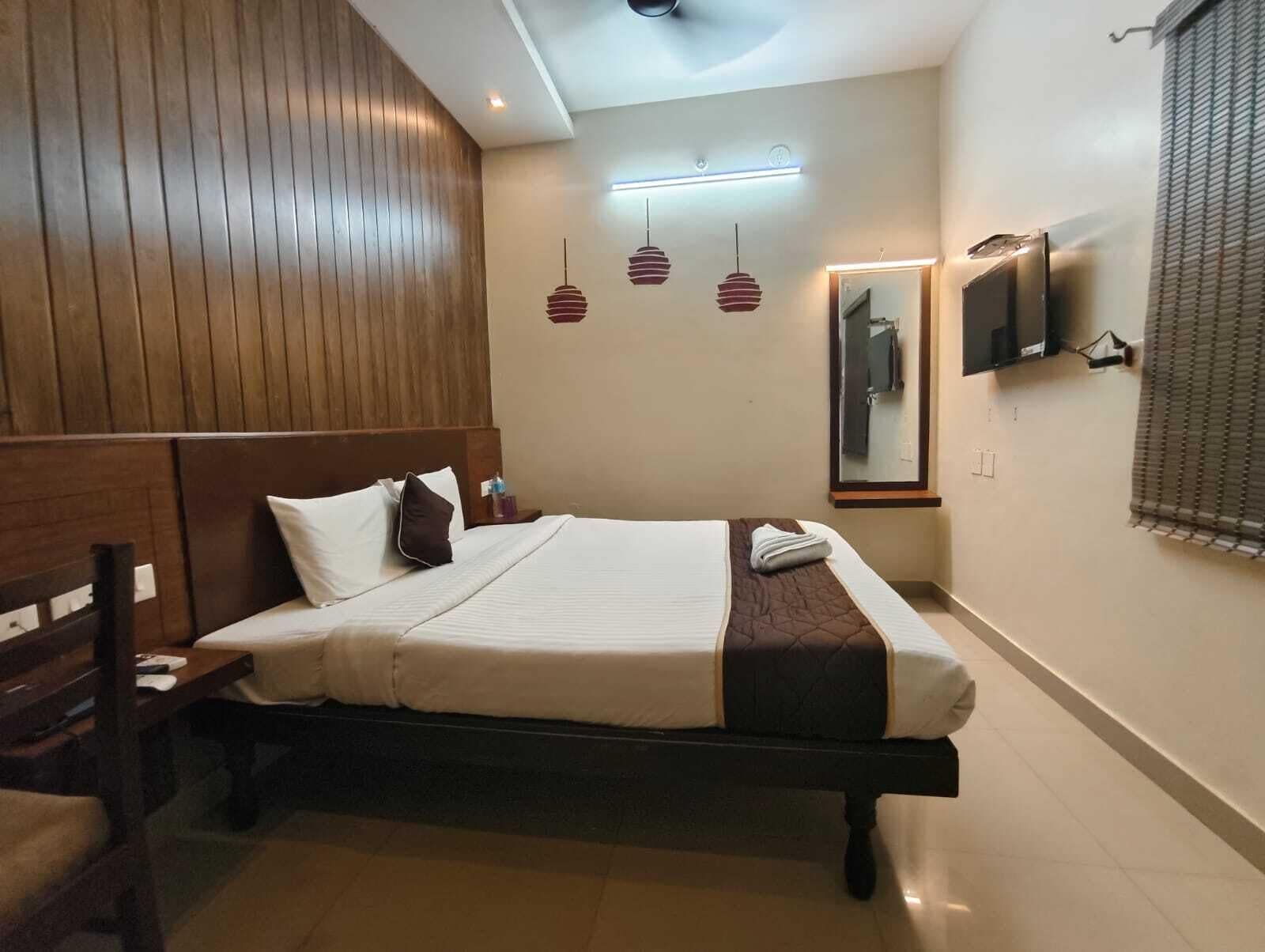 Habitación de hotel con cama, cabecero de madera, mesita de noche, televisor montado en la pared y un espejo.