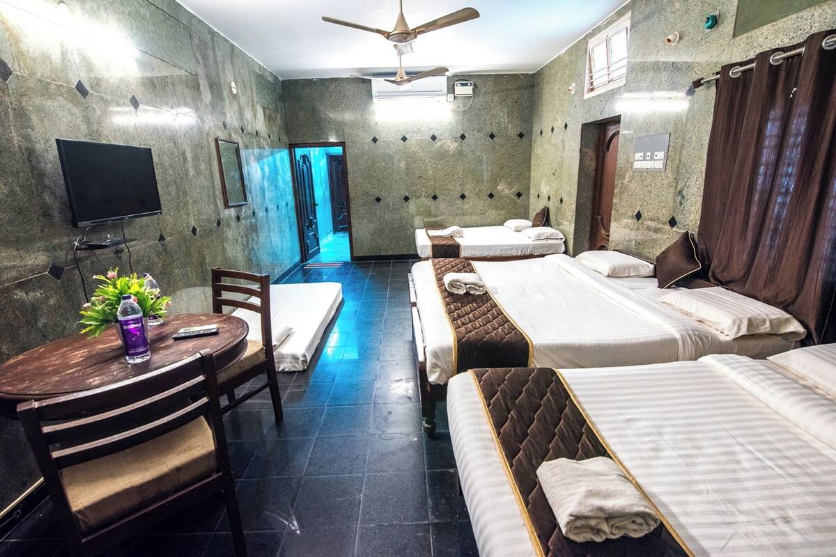 A hotel room with two beds, a desk with a chair, a TV, and a ceiling fan.