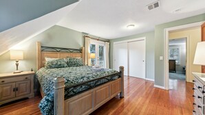 A bedroom with a wooden bed, a nightstand, a dresser, a door, and a ceiling vent.